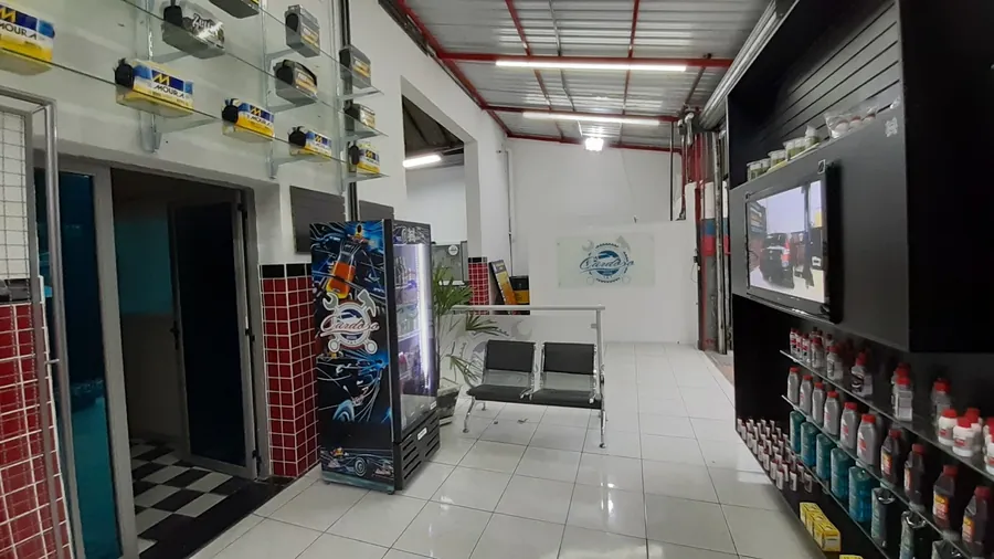 Sala de espera da Oficina Cardoso, com assentos, TV e a placa na parede