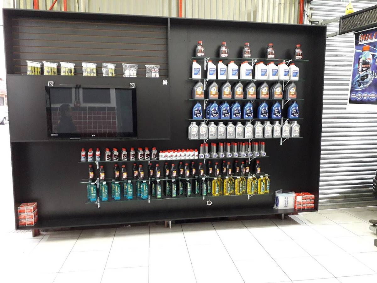 Parede preta de produtos da oficina, com prateleiras de óleo lubrificante, aditivos e filtros organizados.