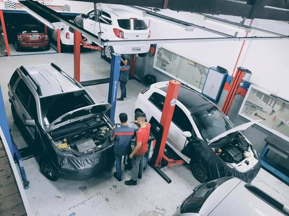 Dois carros em elevadores lado a lado com funcionários trabalhando embaixo deles.
